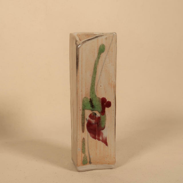 A striking handmade studio pottery bud vase featuring a tall, architectural rectangular form with a softly pinched,...