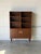 This architectural shelving unit features upper open shelves and lower cabinet doors. Elevated on round tapered legs, it...