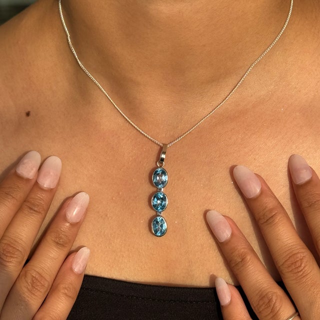 This exquisite sterling silver pendant features three shimmering oval Blue Topaz gemstones (7.49 carats total), each...