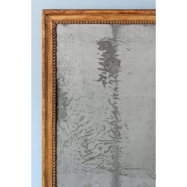 A late 18th-century French gilt gesso mirror, c. 1780, in the Louis XVI style. Of understated rectangular form, the mirror...