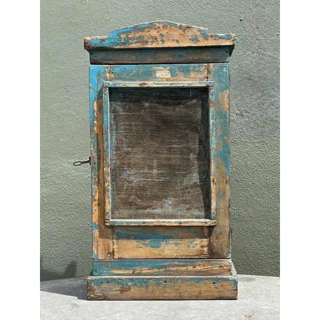 Crafted with a simple, utilitarian silhouette, this vintage rustic cabinet features a wire mesh screen front door topped...