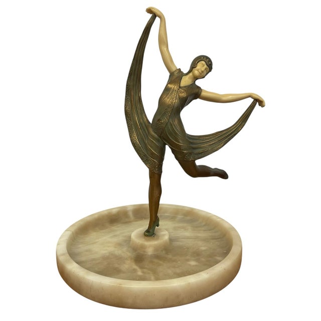 Art Deco style figural sculpture depicting a dancer in a flowing pose mounted at the center of a circular marble dish. The...