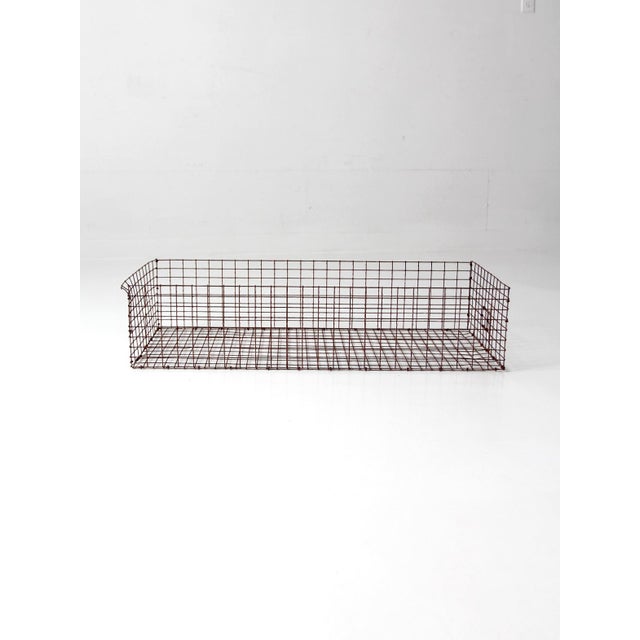 A vintage industrial wire basket with an elongated rectangular form, sloped front, and naturally aged iron finish. The...