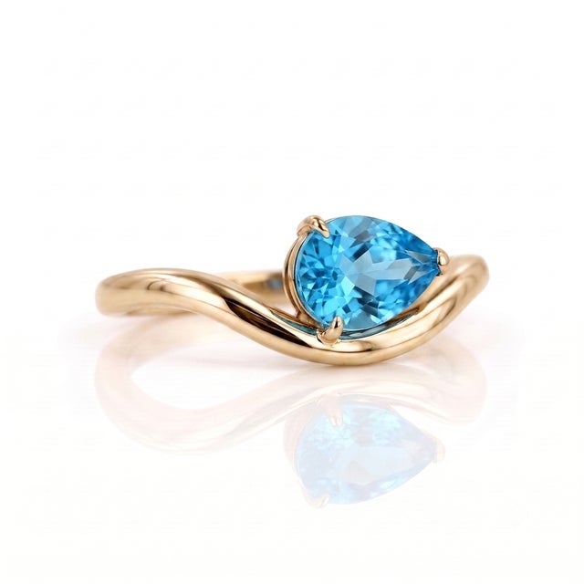 Elevate your everyday style with a touch of modern sophistication. This ring features a vibrant, pear-cut Swiss Blue Topaz...