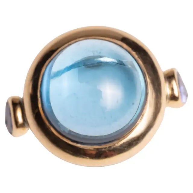 A large round cabochon blue topaz gemstone ring with two faceted, pear-shaped tanzanite stones on the side. 18K gold over...