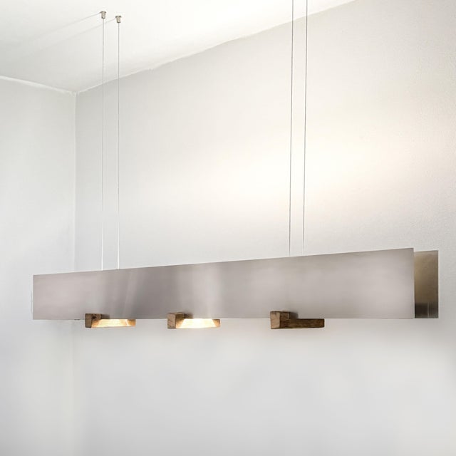 Delicate Aluminium Elements "slicing" through three Wooden Carriers. The outer Elements are larger in size, while the...