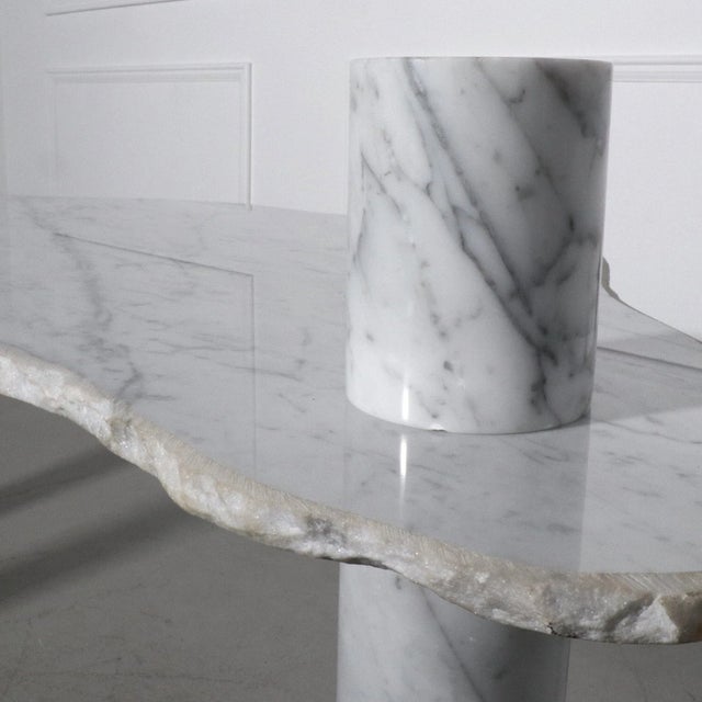 Modern and Rare. Carrara marble table with an organic live edge table top and thick cylinder legs that transverse the...