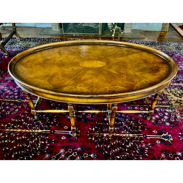 A vintage oval coffee table attributed to Theodore Alexander in a richly-figured burl and satinwood veneer arranged in a...