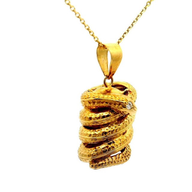 A striking pendant featuring a meticulously crafted golden snake. The snake is intricately coiled, showcasing detailed...