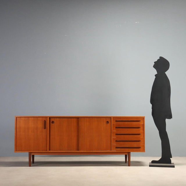 1960s sideboard featuring a functional design typical of the era. Made from teak veneer wood, it offers a refined...