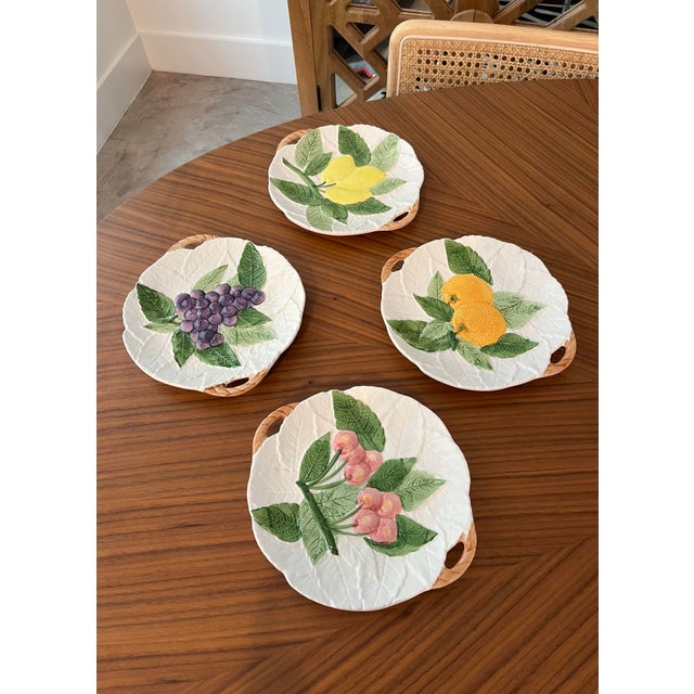 A set of 4 ceramic Fruit du jour plates featuring hand-painted lemons, oranges, cherries and grapes nestled into a...