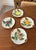 A set of 4 ceramic Fruit du jour plates featuring hand-painted lemons, oranges, cherries and grapes nestled into a...