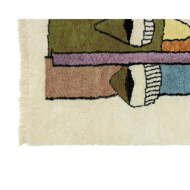 Striking hand-knotted wool rug featuring an abstract face design with accents in Olive Green, Dusty Pink, Burnt Orange,...
