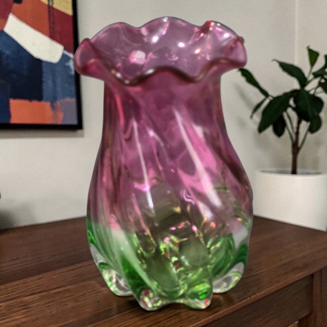This vintage art glass vase features a two-tone design of cranberry and green, with a ruffled top adding a touch of...