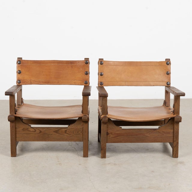 Pair of mid-century Spanish Brutalist club chairs, constructed with substantial dark oak frames and vintage cognac saddle...