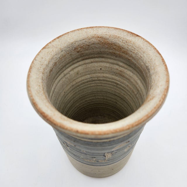 Hand-thrown stoneware vase with sgraffito scroll motif in a blue-gray glaze band, cream body, flared rim, and signed base.