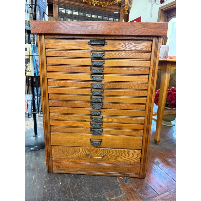 Antique oak printer’s cabinet featuring multiple shallow letterpress type drawers with decorative cast-metal label pulls...