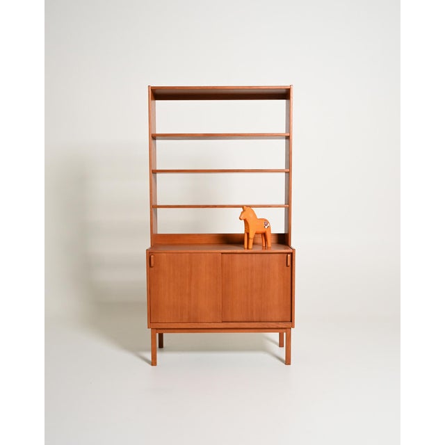 Teak bookcase with open upper shelving and a lower cabinet with sliding doors. Swedish production, 1950s/1960s. Made in...