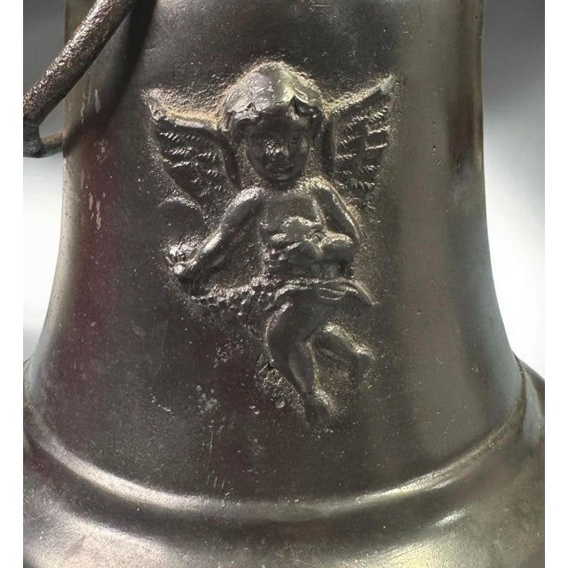 A decorative cast bronze bell featuring a detailed relief of a winged cherub or angel on its exterior. Very heavy piece...