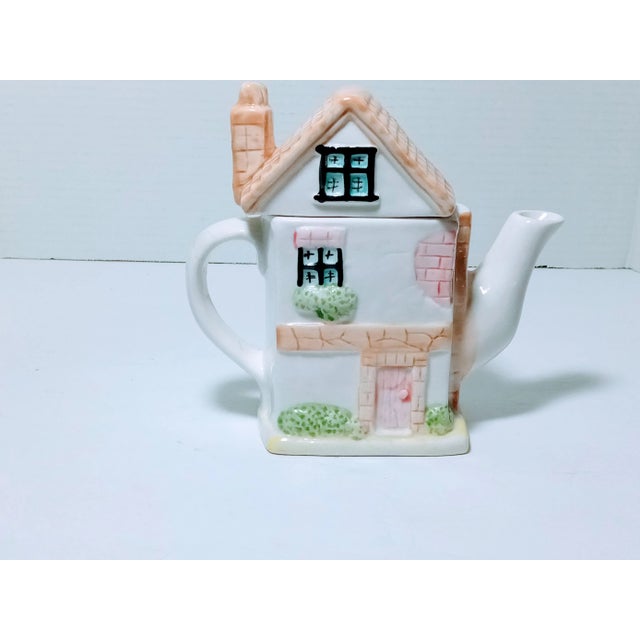 Charming two piece teapot made in China. It has shrubs, windows, and a sign that says Tea Shop. It measures roughly 6 1/2...