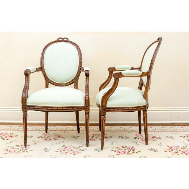 A refined pair of French Louis XVI Revival fauteuil armchairs crafted in warm-toned fruitwood and dating to the early...