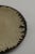 Wheel-thrown plate with a gently curved form, finished in a crackled cream glaze with a dark, irregular edge. Subtle...