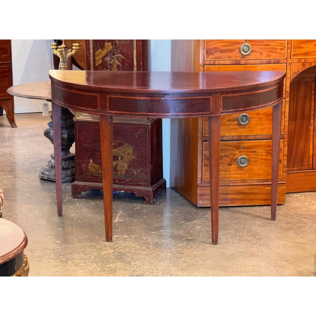 A classic George III demi-lune in mahogany with satinwood and ebony checkered stringing to the apron panels and tapered...