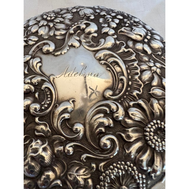 An Antique round handles hand mirror with a beveled mirror. The mirror is sterling silver in an ornate floral repousse...