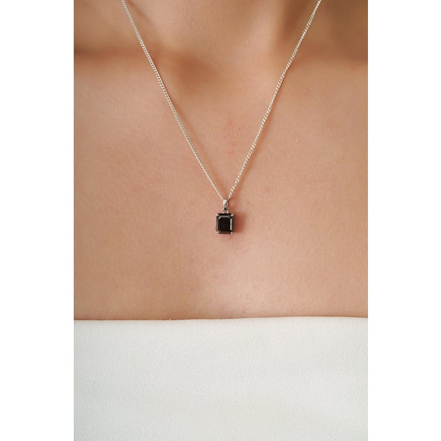 This modernist pendant features a striking 2.69 carat emerald-cut black diamond set in 14K white gold. The diamond...