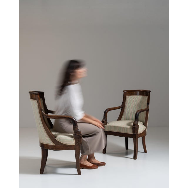 This pair of 19th century Empire upholstered armchairs from France, made in dark mahogany with scrolled arms and cream...
