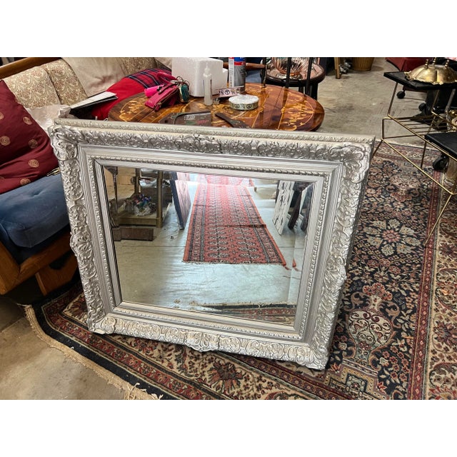This framed mirror, with its understated silver design, serves as a practical and visually appealing element for interior...