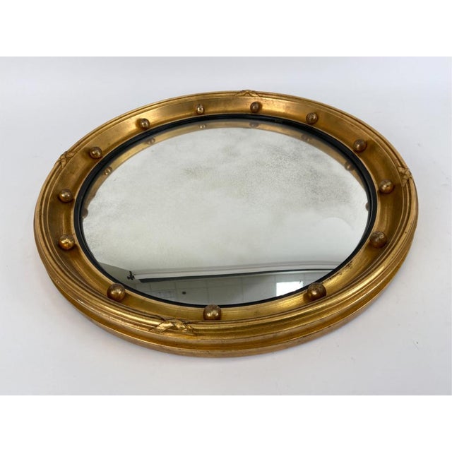A round giltwood Regency style convex bullseye mirror—sometimes called a porthole mirror—with a broad, reeded gilt frame...