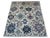 Oversized flowers in denim blue, deep teal, lavender, and pale aqua spread across the ivory field of this handmade Oushak...