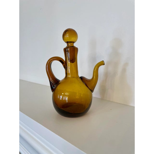 This vintage amber glass blown pitcher is crafted beautifully with a removable stopper. Its amber color varies from light...