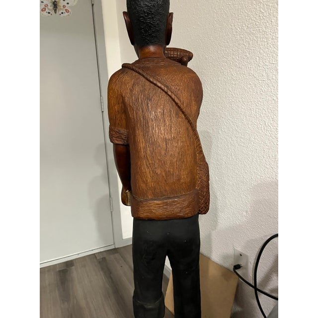 Large wooden hand carved statue depicts, a 1913 Haitian man holding corn cob. Roughly 4 1/2 feet tall.