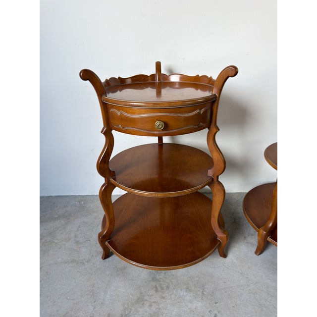 A beautiful pair of vintage Grosfeld House three-tier side tables crafted in a warm walnut finish. Each table features a...
