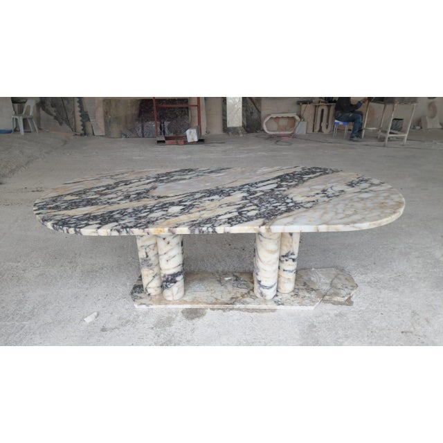 This minimalist table is crafted from striking Viola-veined marble, featuring an elegant oval tabletop that rests...