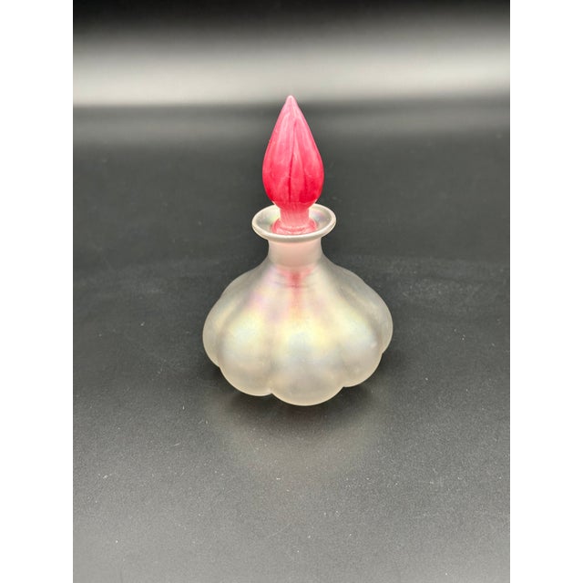 A beautifully crafted iridescent art glass perfume bottle featuring a scalloped, pearlescent base and a striking red...