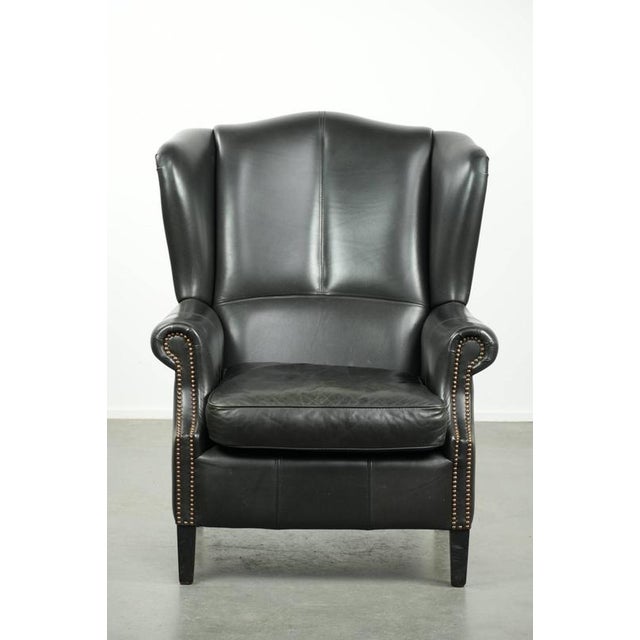 Black cowhide wing armchair in a classic English style, finished with decorative studs. : This black cowhide wing armchair...