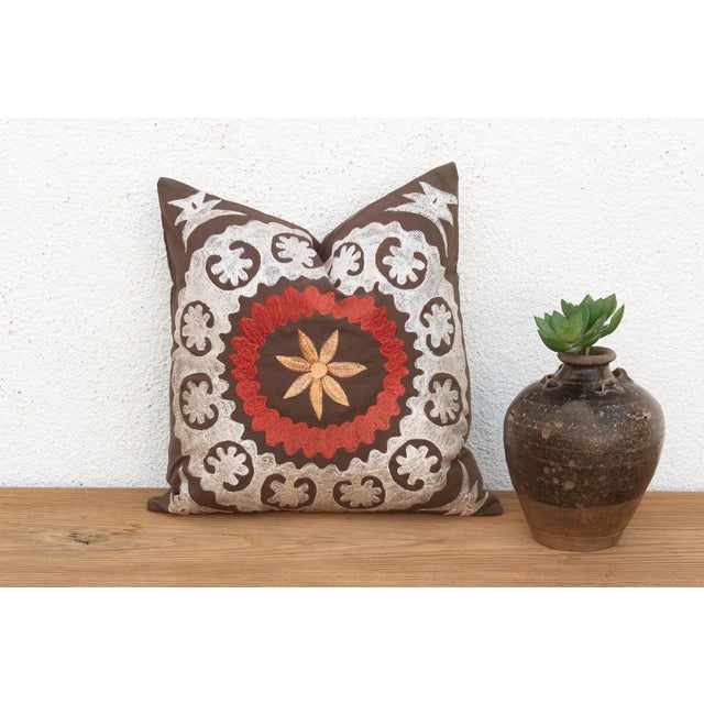 A large floral medallion in raised, hand-embroidered satin stitch anchors the center of this pillow — radiating palmette...