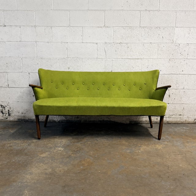 A vintage Danish sofa dating to the early 1950s, with a sculptural winged back, slender teak arm caps, and gently splayed...