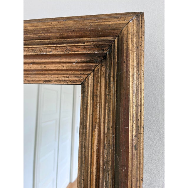 An antique French giltwood wall mirror, dating to the late 19th century. This rectangular mirror has a warm gold frame...