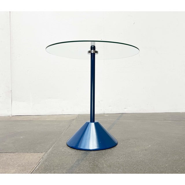 Postmodern side table with a heavy base and glass tabletop. The round glass tabletop is secured to the stem by two chrome-...