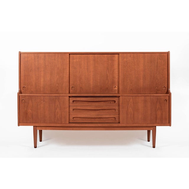 This vintage mid-century Danish modern tall teak wood sideboard server or bar cabinet attributed to Johannes Andersen for...