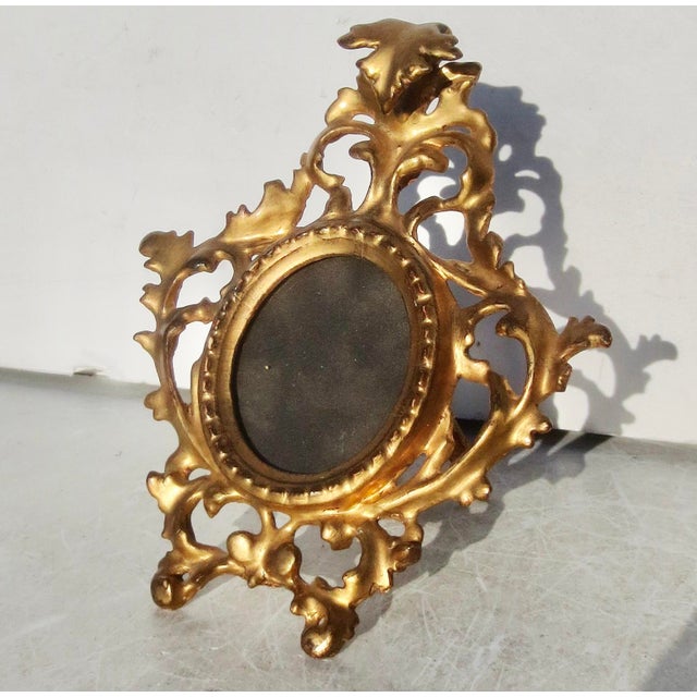 Finely carved and gilt wooden oval frame. Baroque scrolling foliage surrounds the oval and is supported by a wooden easel...