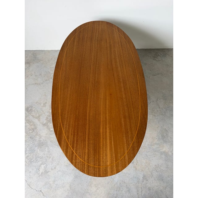 Elegant 1960s Hollywood Regency coffee table crafted in rich mahogany with a classic oval top featuring a subtle inlaid...