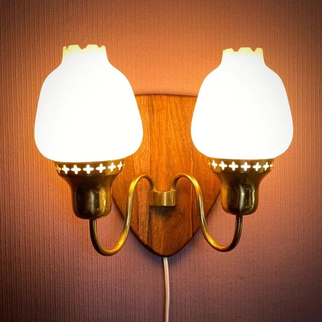 A wall lamp made from brass with two arms mounted on a solid teak panel. Perforated pattern with decorative stars....