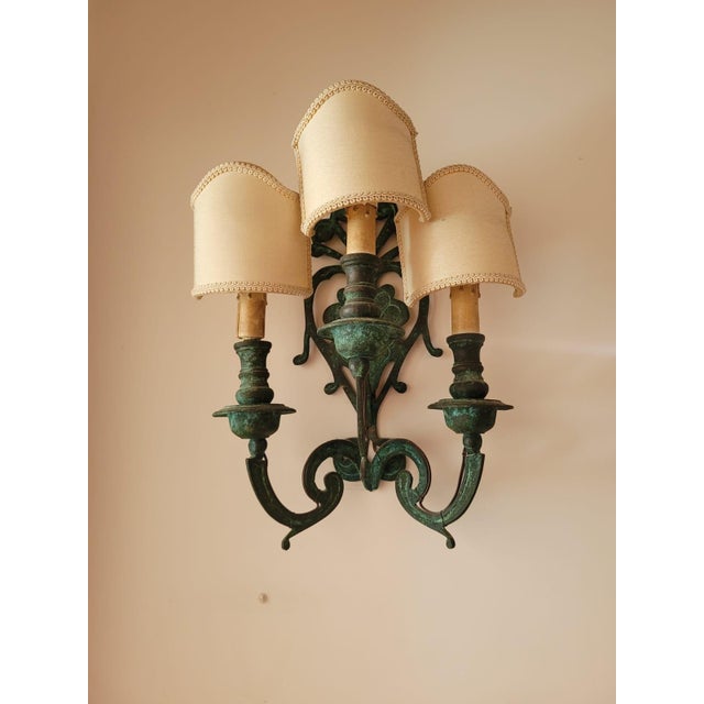 A pair of vintage bronze three-light wall sconces, featuring an antiqued green patina finish. The curved arms and...