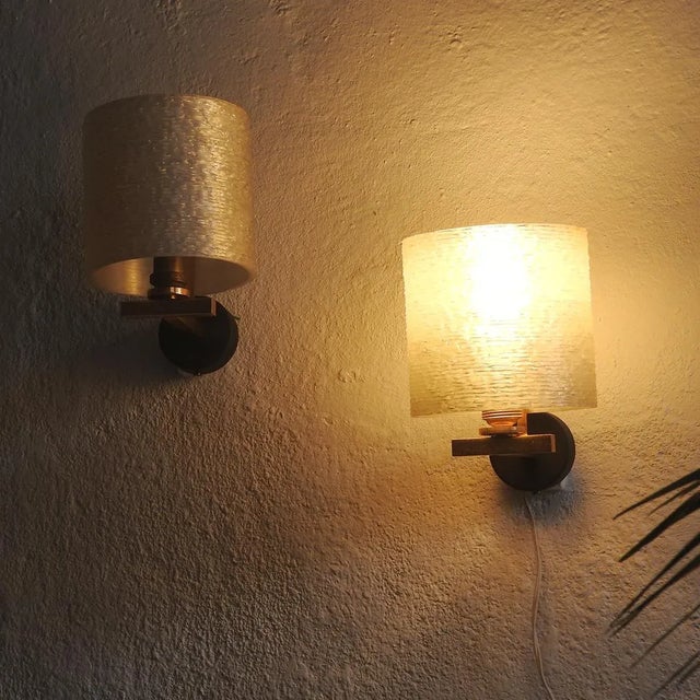 Black metal and gold-plated brass wall lamps with a cylindrical resin shade with a textured, pearlescent sheen. They...