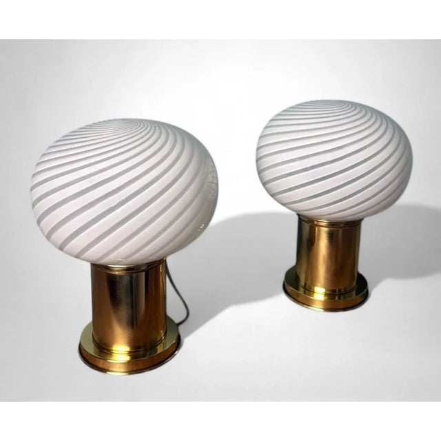Elegant pair of vintage table lamps featuring a handblown Murano glass sphere resting on a solid cylindrical brass base....